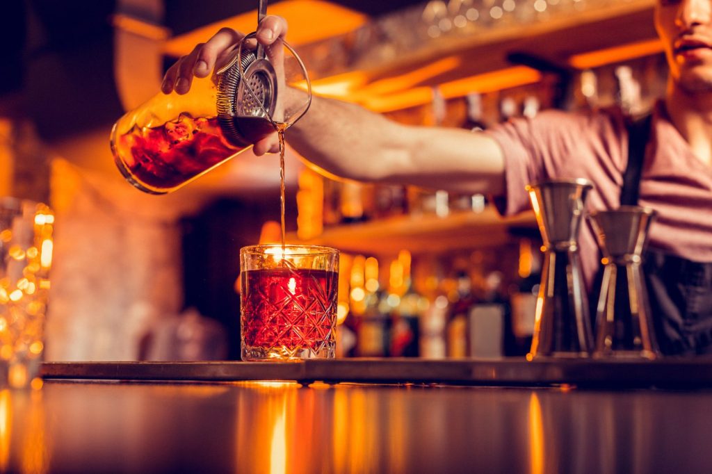 How to price cocktails: bartender pouring a stirred cocktail next to two jiggers on the bar