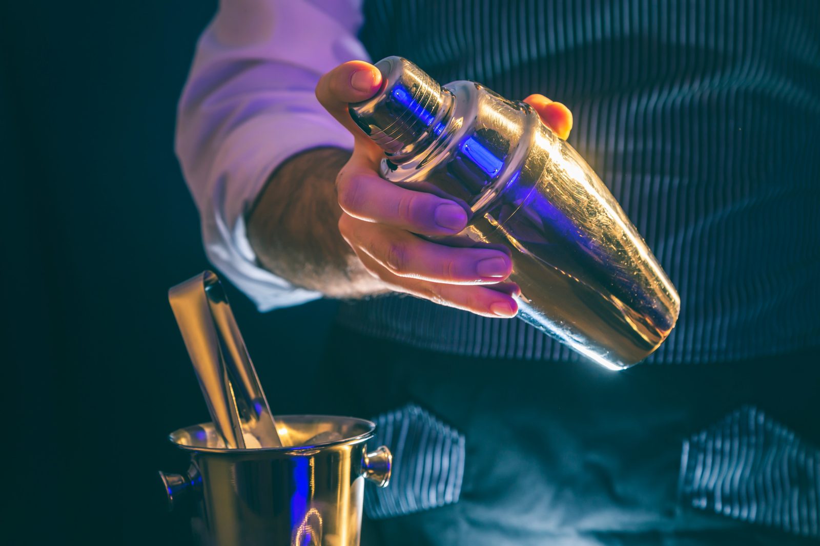 Bartender holding a cocktail shaker over an ice bucket, part of costing every ingredient when you price cocktails