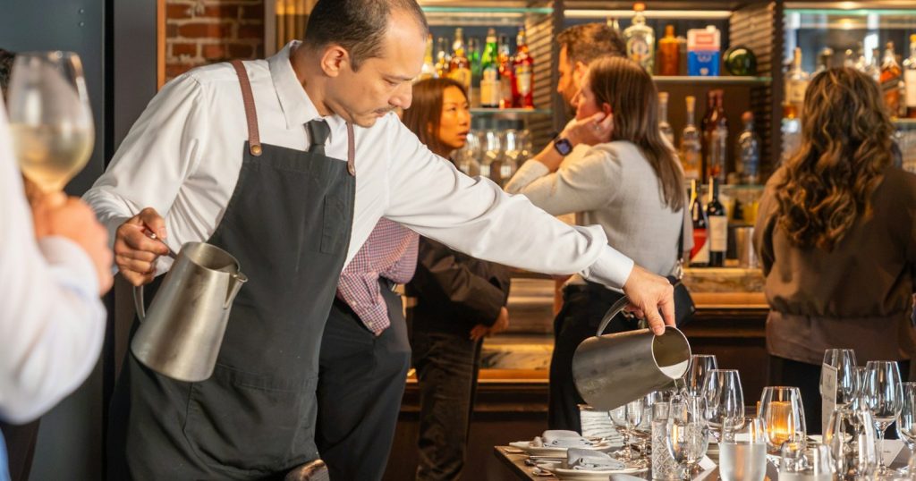Server pouring water for guests during a restaurant soft opening